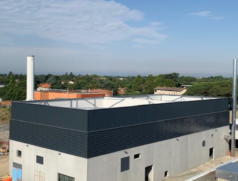 Écran acoustique en bardage sombre installé en périphérie de la toiture d'un bâtiment technique, masquant les équipements et leurs cheminées