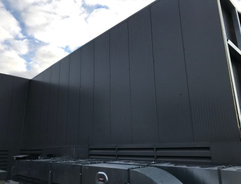 Vue rapprochée d'un écran acoustique en bardage sombre installé devant un groupe de ventilation, avec grilles de reprise d'air en partie basse