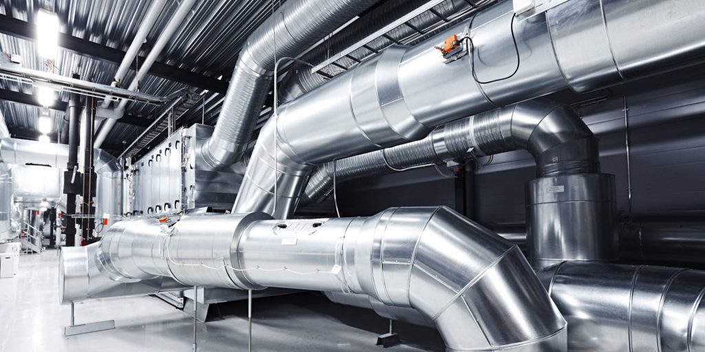 Réseau de gaines de ventilation galvanisées de grande section dans un local technique industriel, avec coudes, piquages et registres motorisés